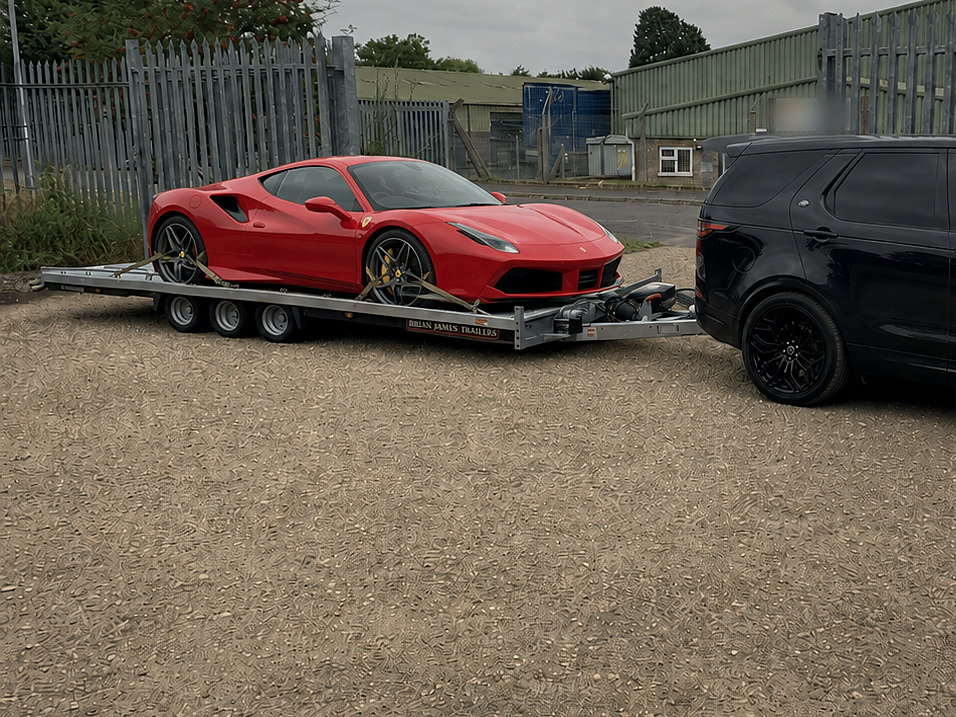 A red Ferrari strapped onto a car trailer behind a black 4x4